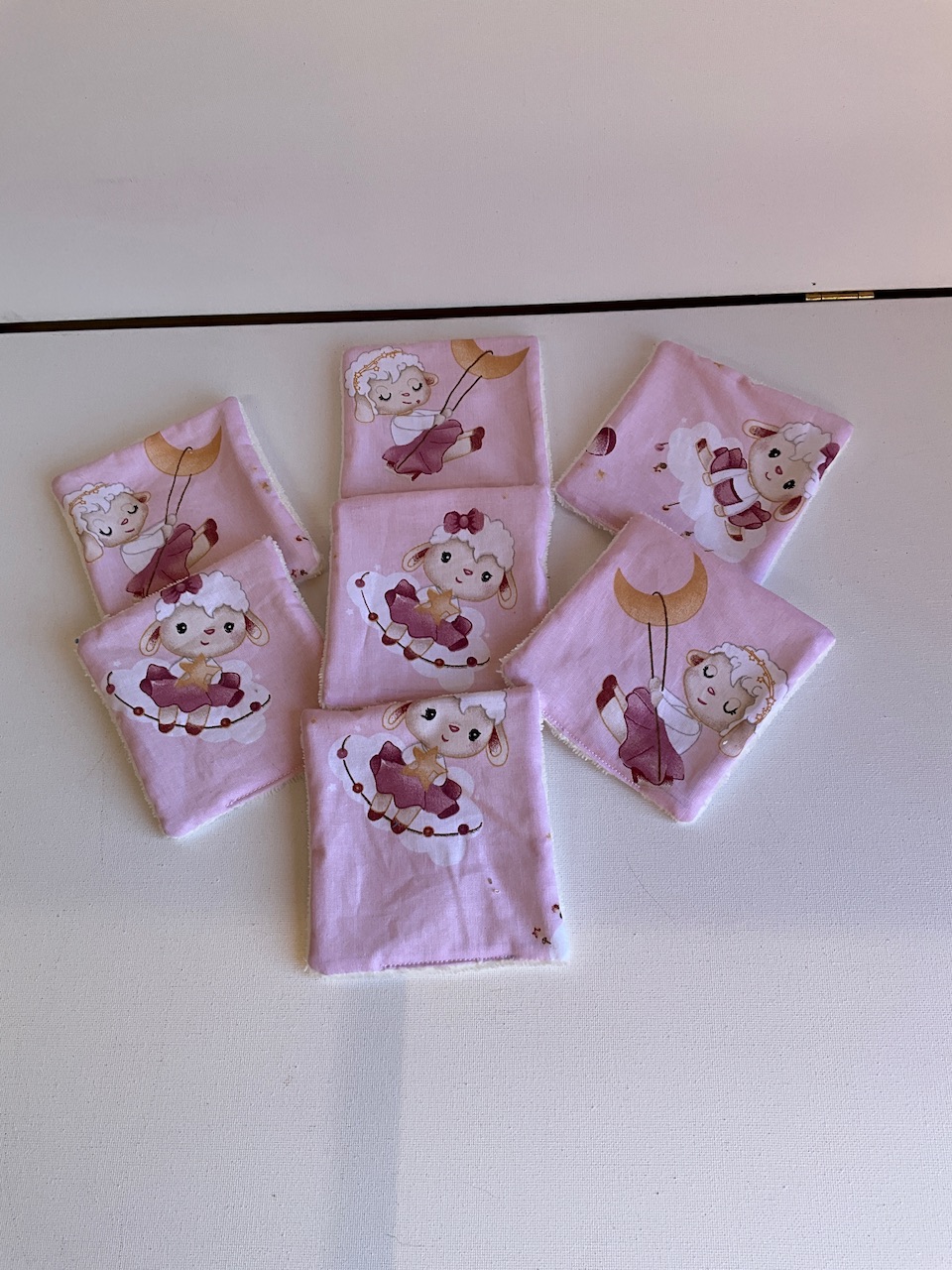 Sept lingettes lavables pour bébé en coton imprimé agneaux danseuses fond rose, étalées en éventail, format 10 x 10 cm