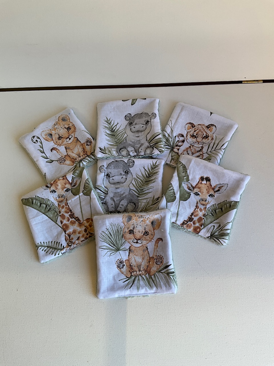 Sept lingettes lavables pour bébé en coton imprimé lionceaux et girafes aquarelle, étalées en éventail, format 10 x 10 cm