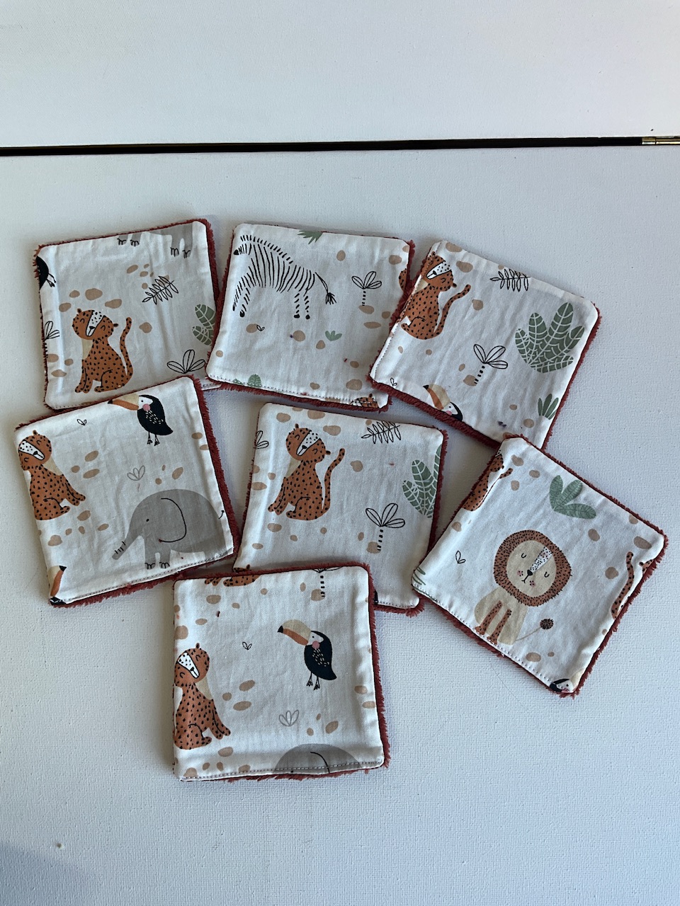 Sept lingettes lavables pour bébé en coton imprimé savane graphique et pois fond écru, étalées en éventail, format 10 x 10 cm
