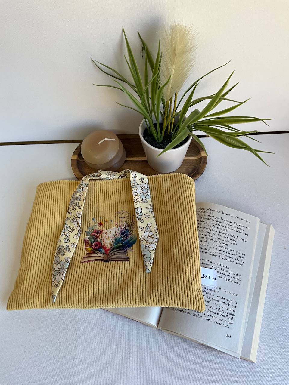 Pochette à livre horizontale en velours côtelé moutarde, appliqué livre fleuri – posée sur un livre ouvert, cousue main par Sidonie Créa