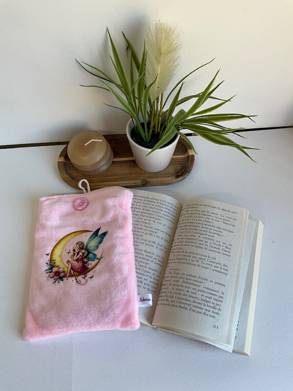 Pochette à livre verticale en velours rose, appliqué fée sur la lune – posée sur un livre ouvert, cousue main par Sidonie Créa
