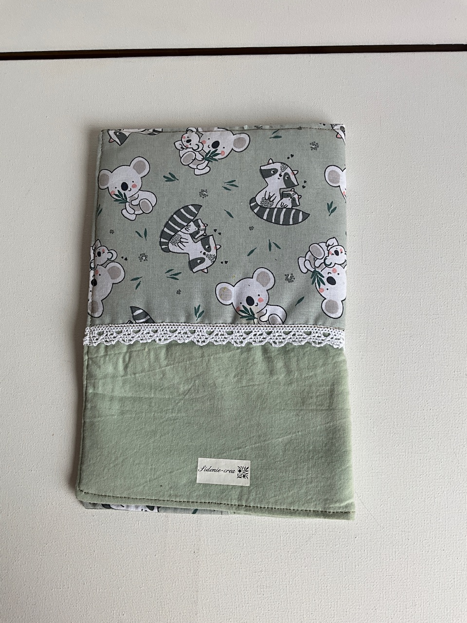 Dos du protège carnet de santé bébé en coton imprimé koalas et ratons laveurs avec bande vert sauge, cousu main dans l’Oise