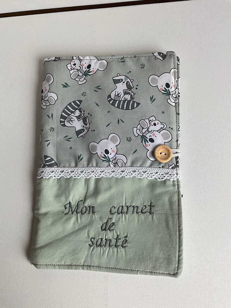 Protège carnet de santé bébé en coton imprimé koalas et ratons laveurs, bande vert sauge brodée « Mon carnet de santé », galon de dentelle et bouton en bois, Sidonie Créa