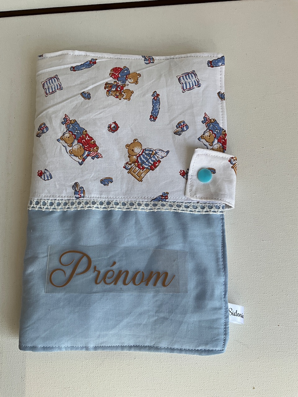 Protège carnet de santé personnalisable en coton oursons et jouets fond blanc – vu de face avec le prénom floqué, cousu main par Sidonie Créa